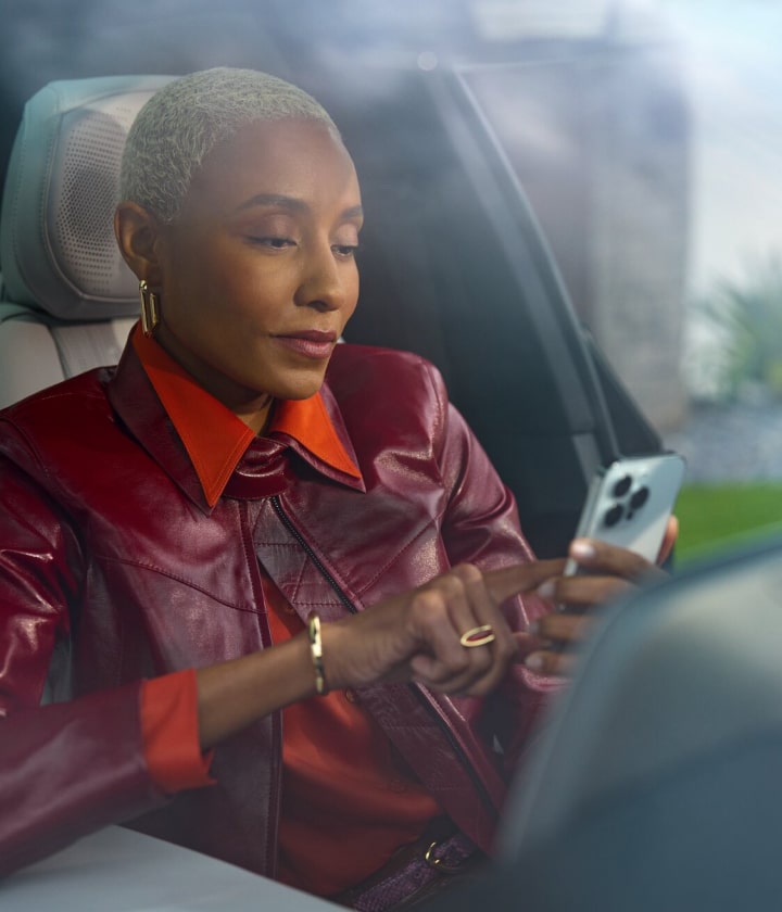 A person seated inside a vehicle using a smartphone to access the OnStar mobile app.