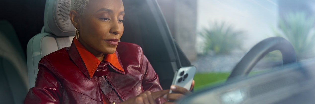 A person seated at a driver's seat using a smartphone to access the OnStar mobile app.