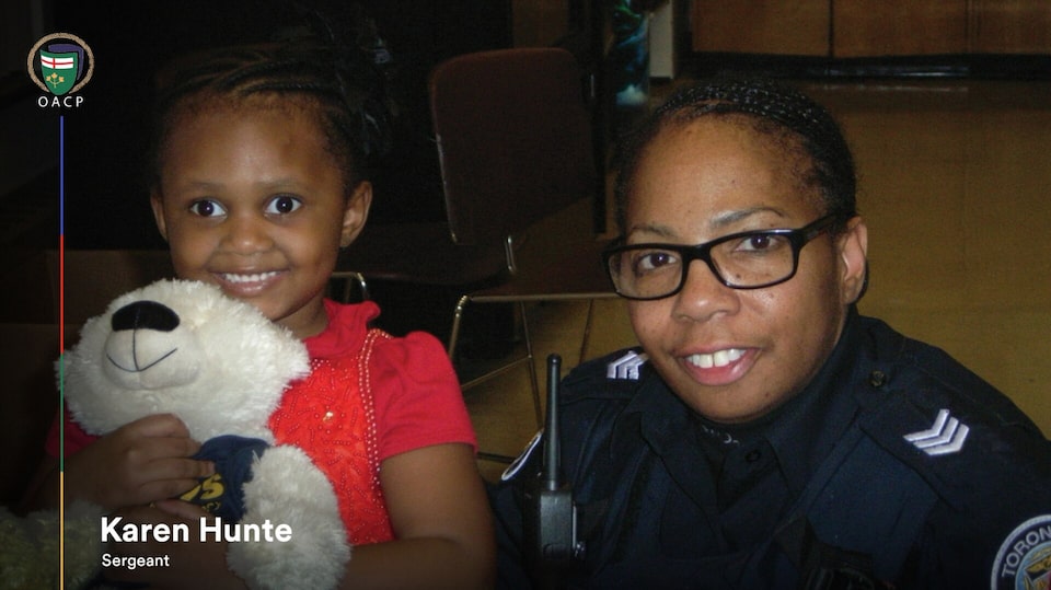 Sergeant Karen Hunte of the Toronto Police Service beside a young child holding a teddy bear.