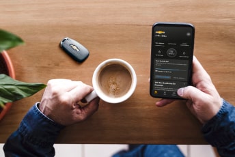 Une personne accédant à l’appli mobile de véhicule OnStar via un téléphone intelligent, tout en tenant un café dans l’autre main.