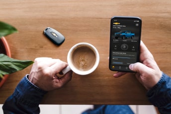 A person accessing OnStar's vehicle mobile app through a smartphone while holding coffee with the other hand.