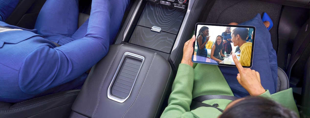 A man and woman in a car with the woman holding a tablet.