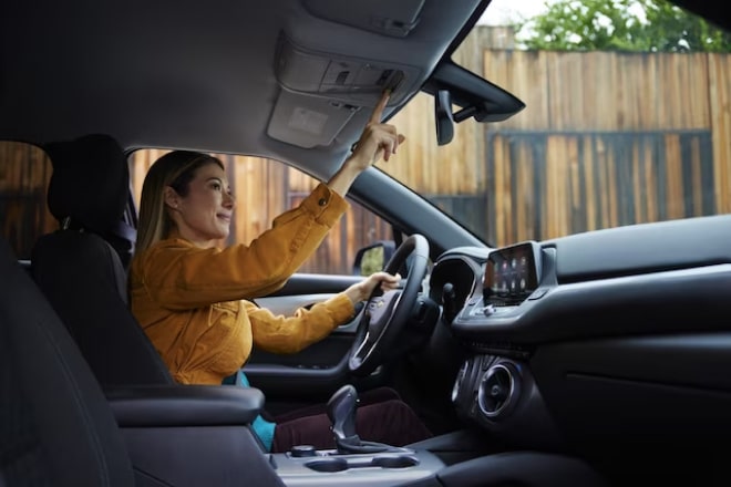 A person in a yellow jacket pressing the OnStar button in her vehicle.