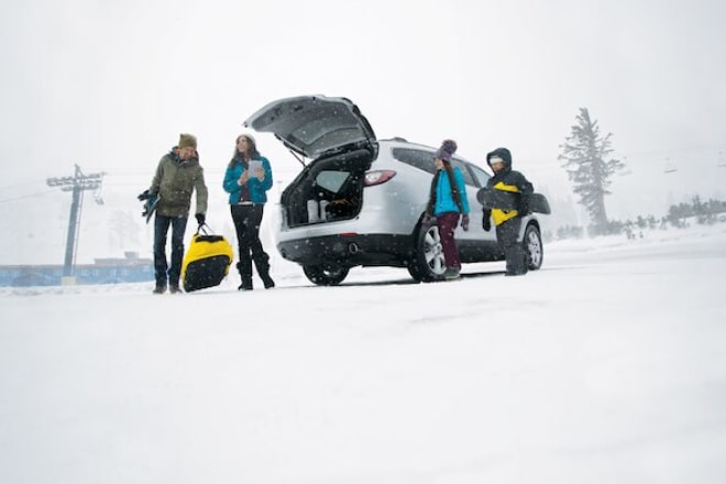 Four people procuring their belongings from a vehicle in the middle of a snowy area.