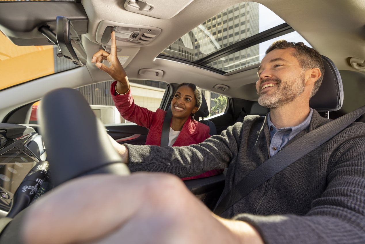 Woman pressing the OnStar button while a man is driving.